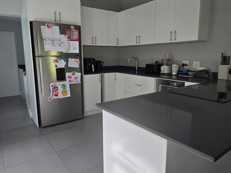 Modern kitchen featuring white cabinetry, dark stone countertops, a central island, and tiled flooring, offering a clean and functional workspace.