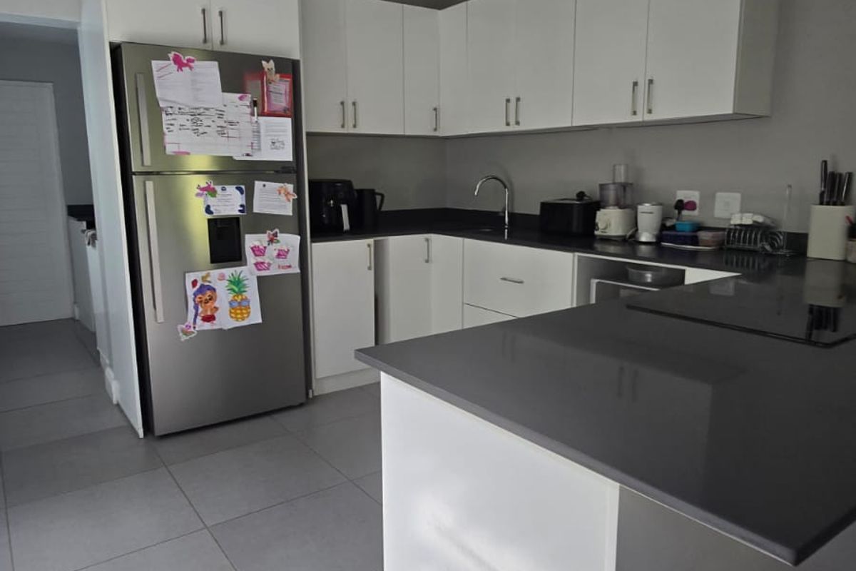 Modern kitchen featuring white cabinetry, dark stone countertops, a central island, and tiled flooring, offering a clean and functional workspace.