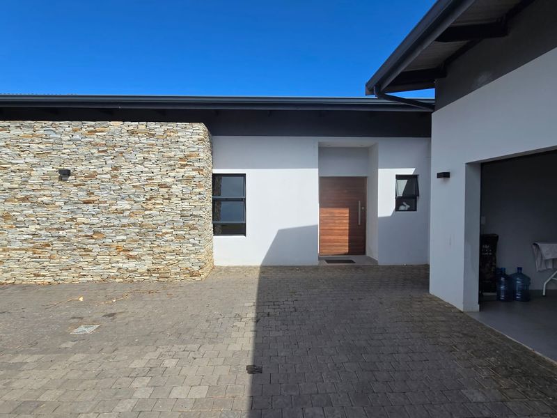 Modern front facade featuring a combination of white render and natural stone cladding, with a timber entrance door and paved driveway leading to a garage.