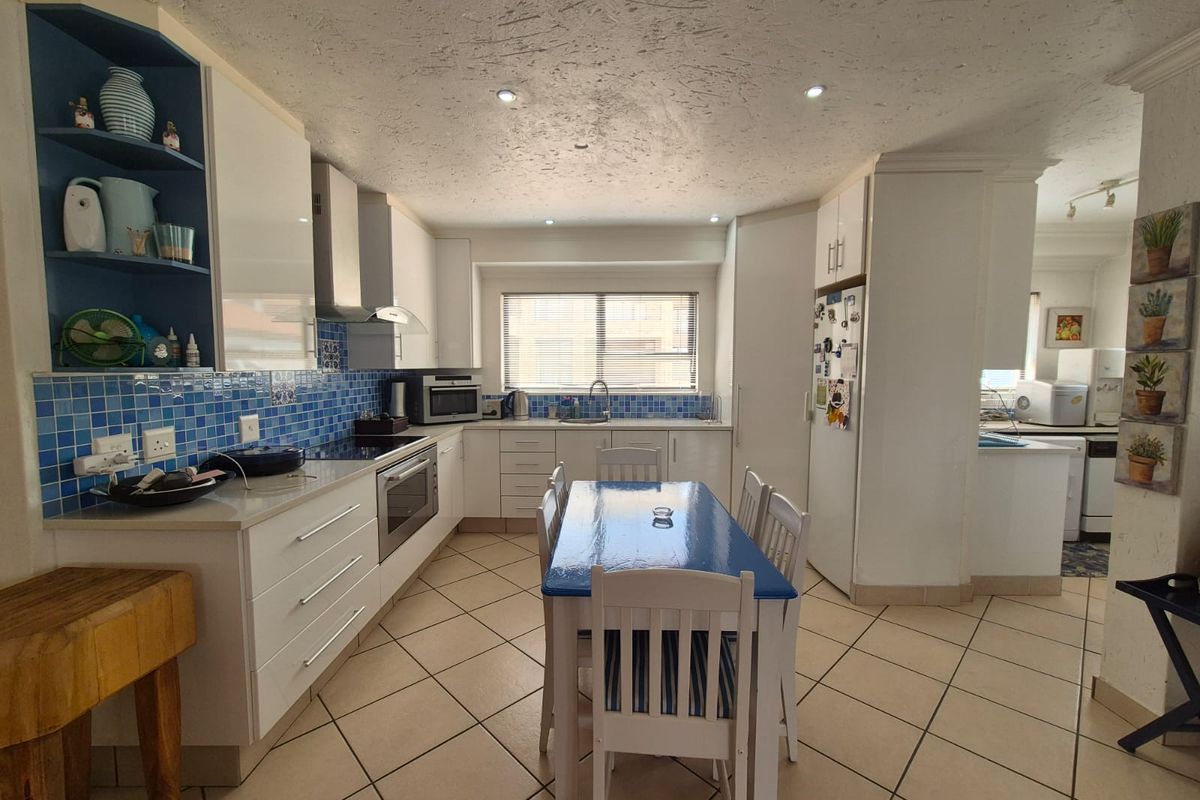 A functional kitchen featuring white cabinetry, blue tiled splashbacks, integrated oven, and a dedicated dining area with tiled flooring throughout.