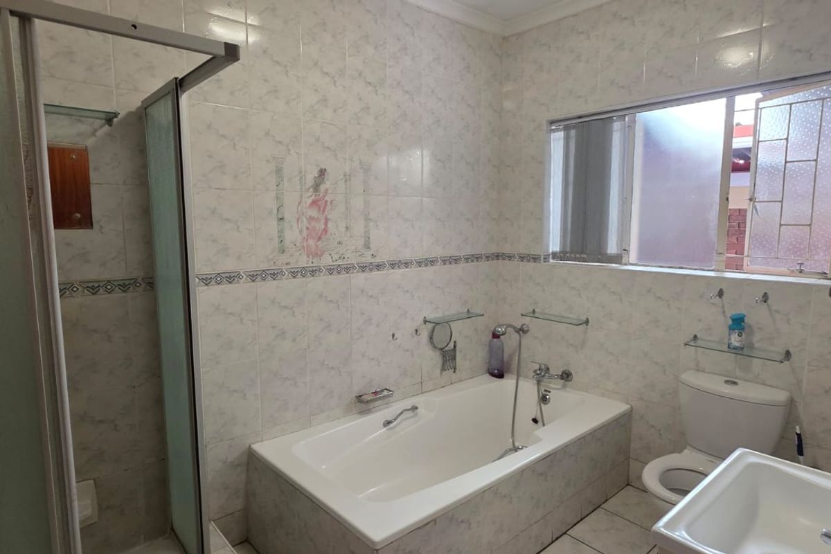 A functional bathroom featuring a built-in bathtub, separate shower enclosure, toilet, and vanity basin with tiled walls and flooring.