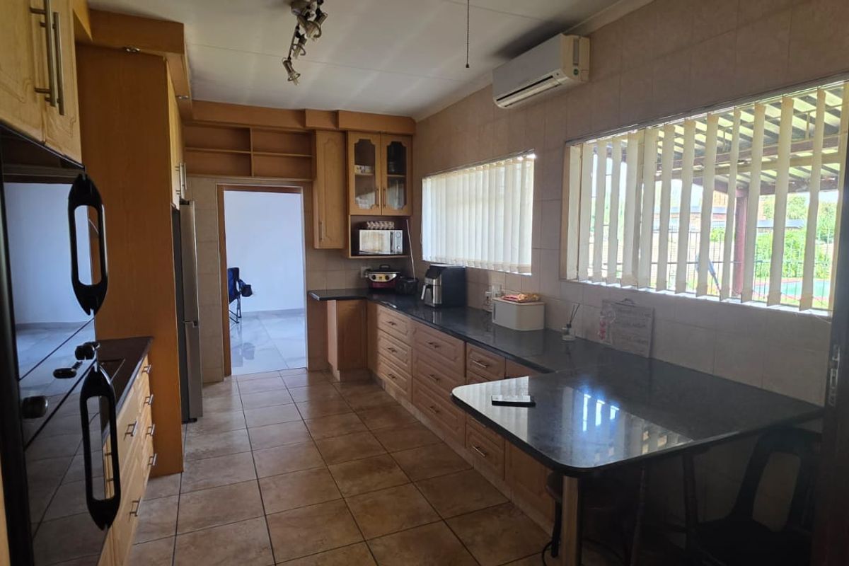 A functional kitchen featuring wooden cabinetry, dark granite countertops, tiled flooring, and a wall-mounted air conditioning unit.