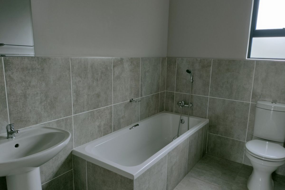 A modern bathroom featuring a tiled bathtub with a handheld shower attachment, a pedestal basin, and a standard toilet.