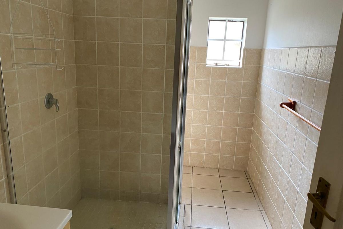 A functional bathroom featuring a glass-enclosed shower, neutral wall and floor tiling, and a small window for natural light.