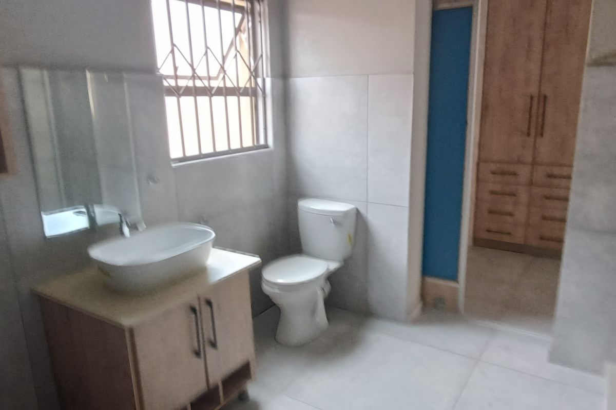 A modern bathroom featuring a vessel sink vanity, a toilet, and large format floor tiles, with an adjacent walk-in closet area.