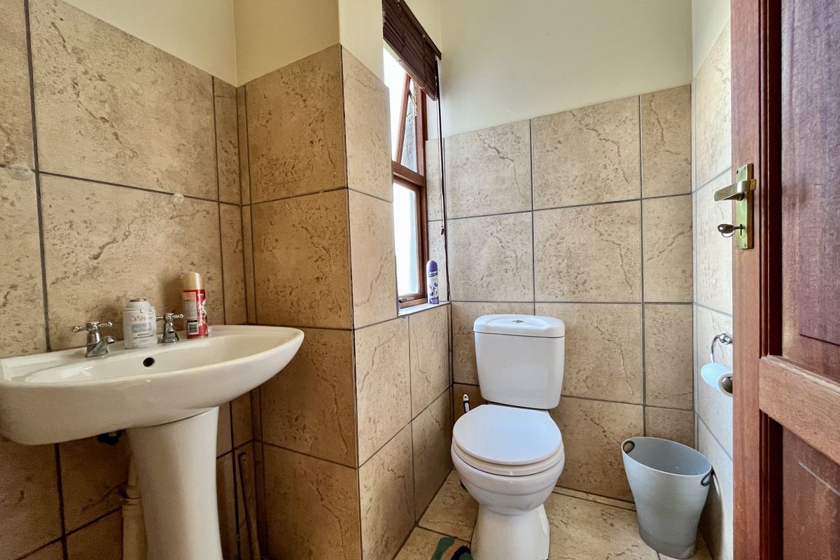 A functional guest bathroom featuring a pedestal basin, a standard toilet, and neutral wall tiling throughout.