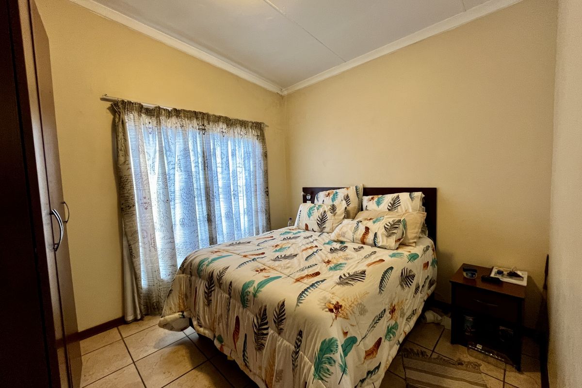 A standard bedroom featuring tiled flooring, built-in cupboard space, and a window with curtain rails.
