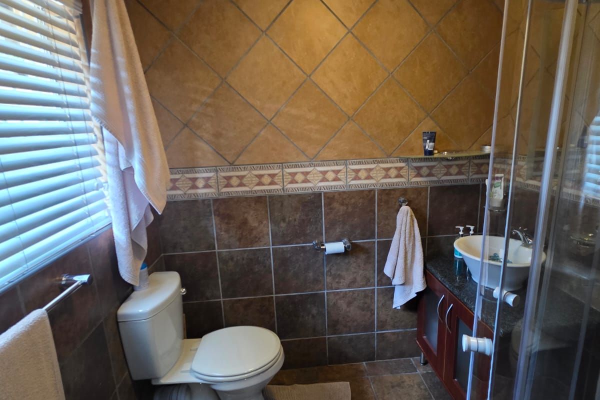 A functional bathroom featuring a corner shower enclosure, a vanity with a vessel sink, and a toilet, finished with earth-toned wall and floor tiling.