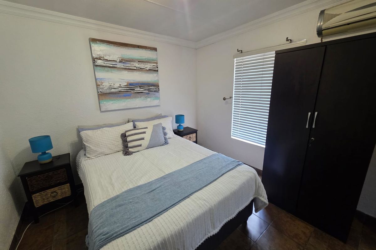 A well-maintained bedroom featuring tiled flooring, a wall-mounted air conditioning unit, and window blinds.