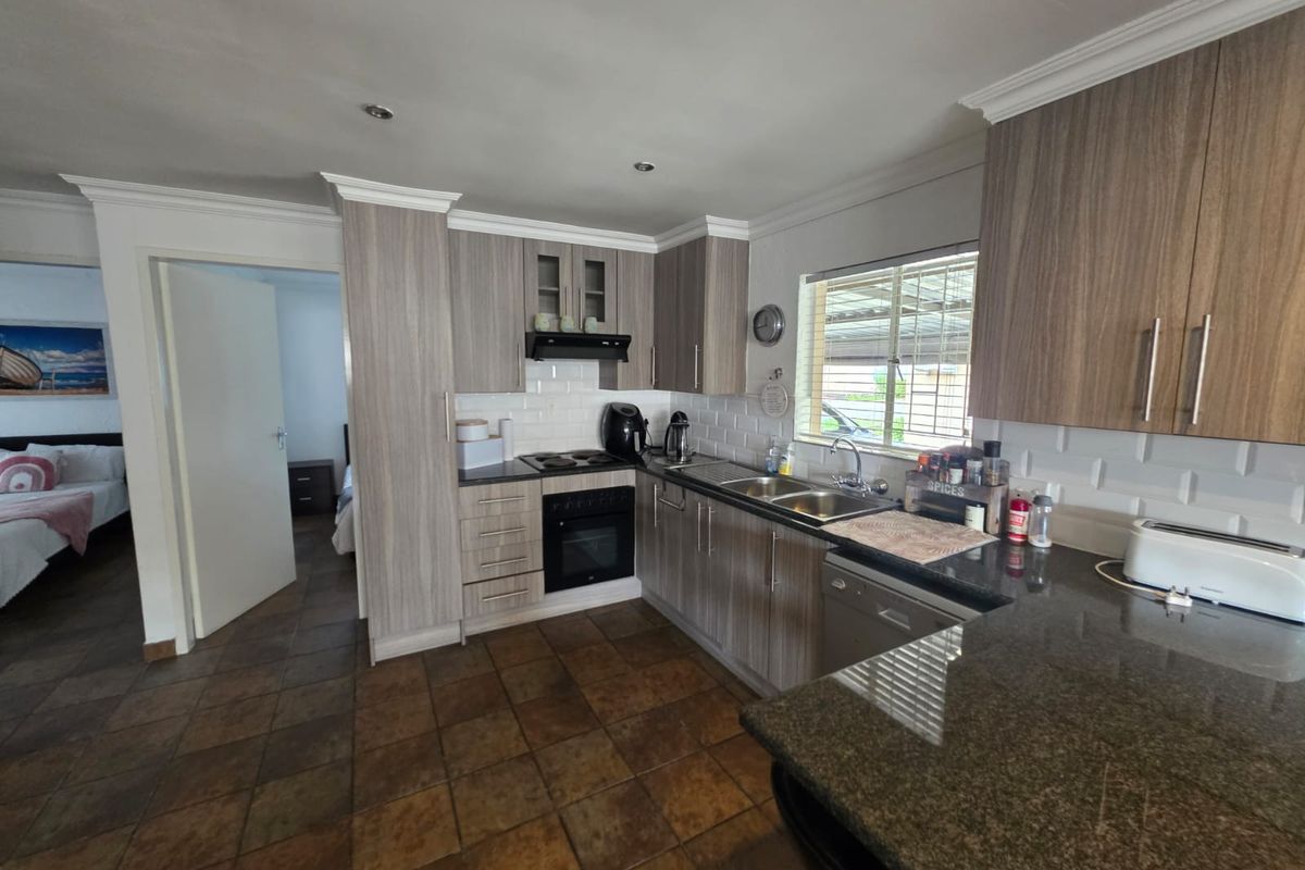 A functional kitchen featuring wood-grain cabinetry, granite countertops, a built-in oven, hob, extractor fan, and a double sink with tiled backsplash.