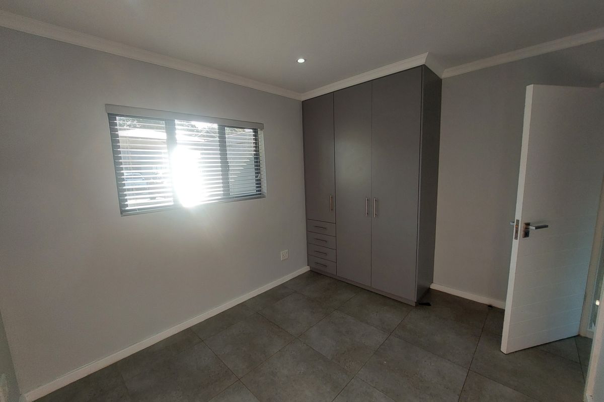 A clean, modern bedroom featuring large-format floor tiles, built-in grey cabinetry, and recessed ceiling lighting.
