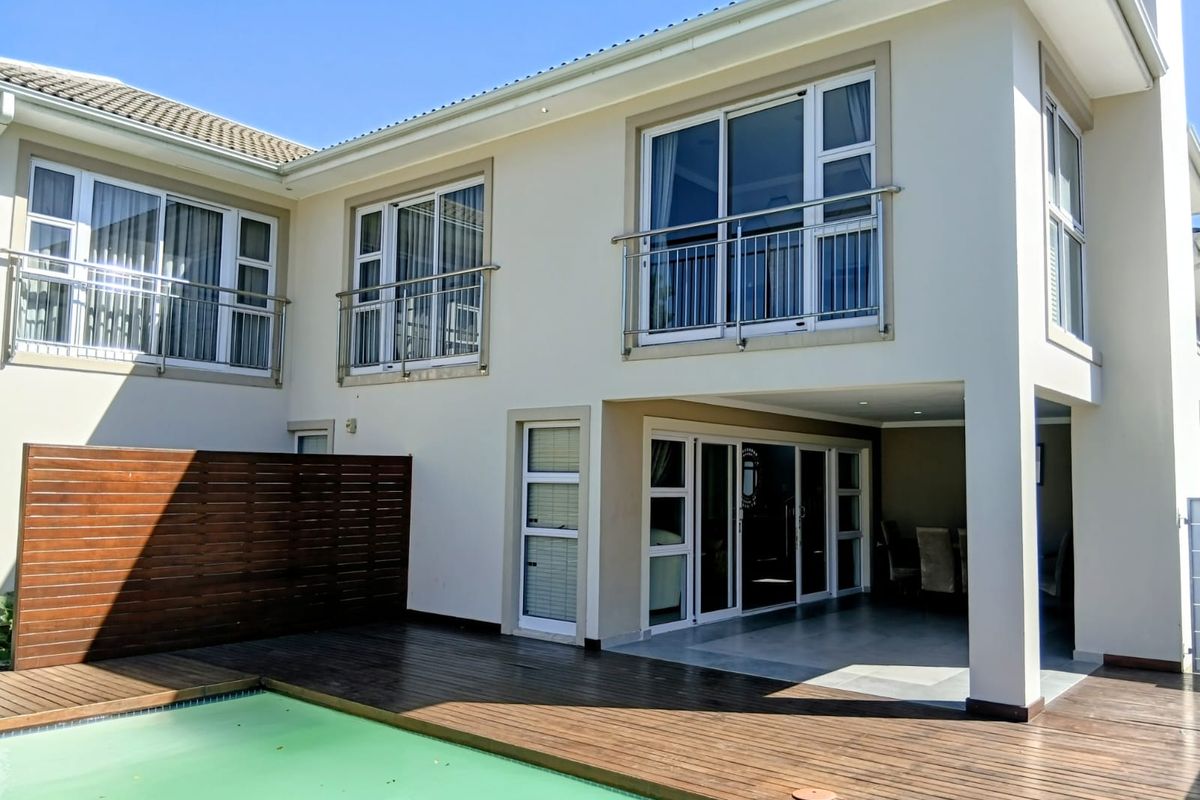 Rear view of the property featuring a swimming pool, timber decking, covered patio area, and upper-level balconies with stainless steel railings.