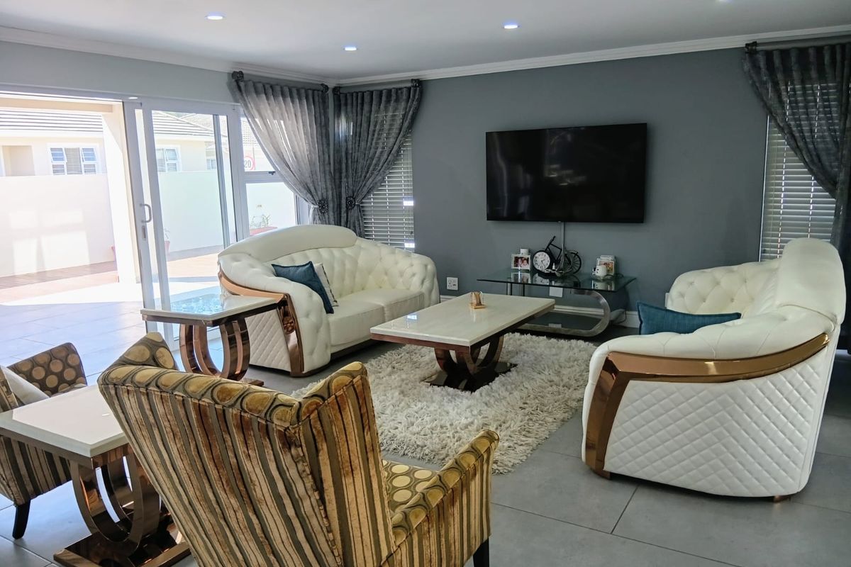 A modern living room featuring large sliding glass doors, recessed ceiling lighting, and neutral tiled flooring, providing seamless access to the outdoor patio area.