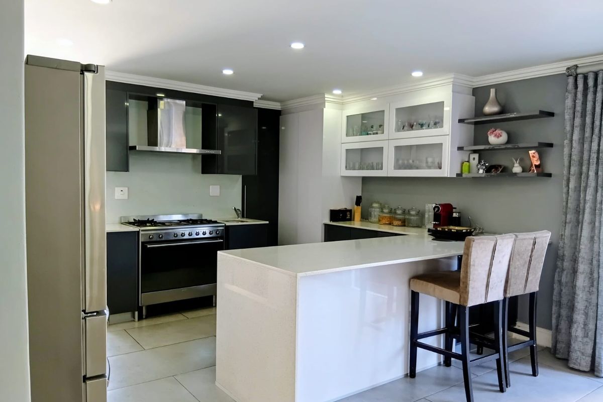Modern kitchen featuring a central island with breakfast bar, sleek cabinetry, stainless steel gas stove, extractor fan, and recessed ceiling lighting.