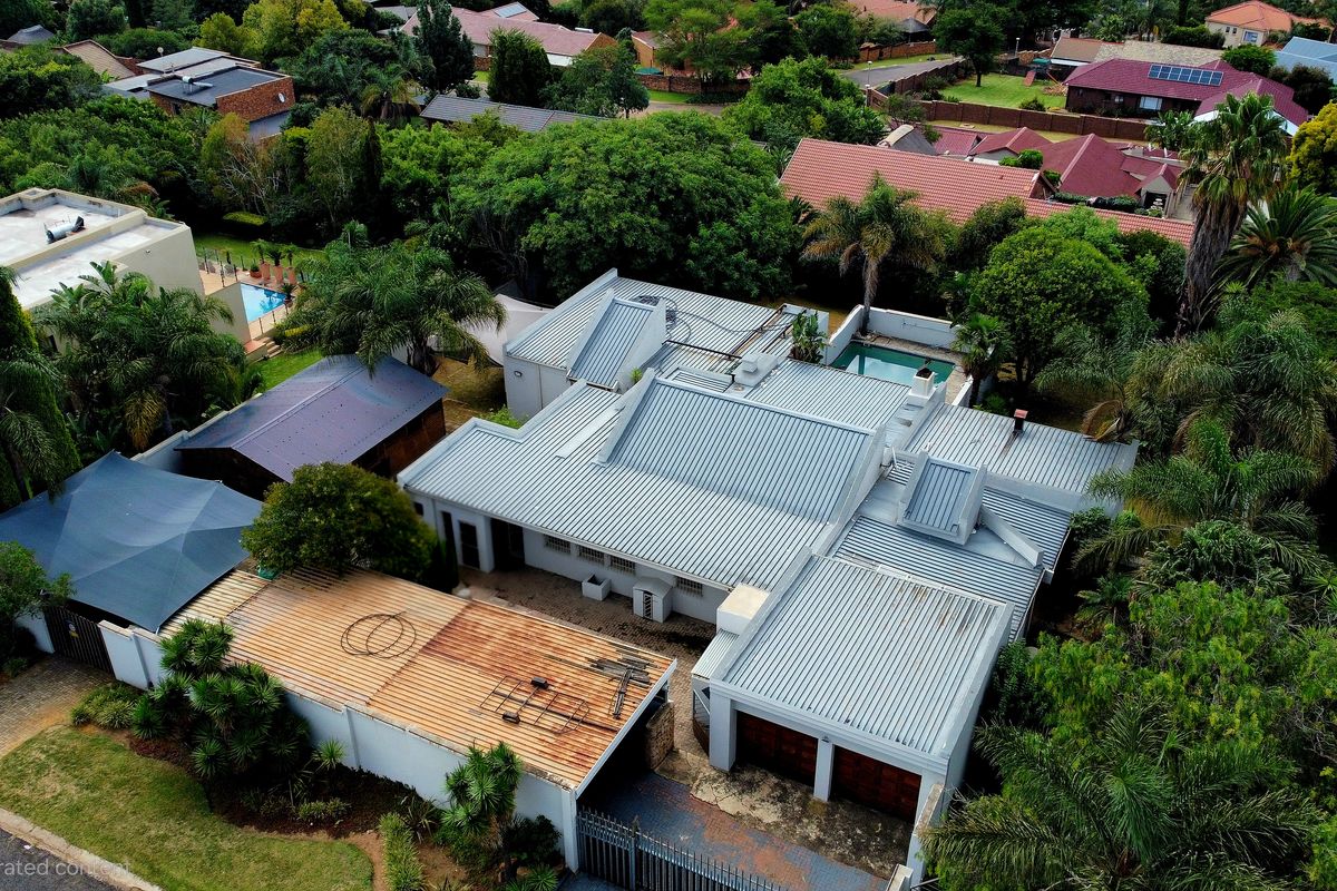 Aerial view of a residential property featuring a corrugated metal roof, a swimming pool, and a double garage within a landscaped suburban setting.