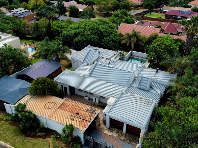Aerial view of a residential property featuring a corrugated metal roof, a swimming pool, and a double garage within a landscaped suburban setting.
