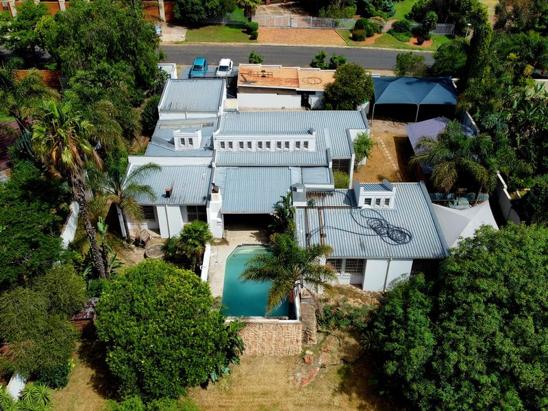 Aerial view of the property showcasing the main dwelling with a metal roof, swimming pool, established garden, and carport area.