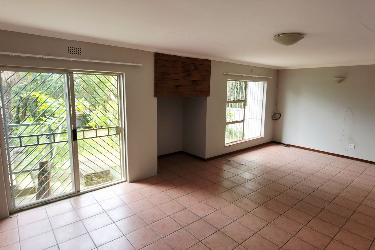An empty living room featuring tiled flooring, a wooden fireplace surround, and sliding glass doors with security bars leading to the garden.