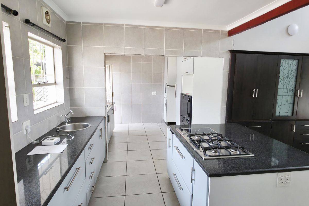 A functional kitchen featuring a central island with a gas hob, granite countertops, ample built-in cabinetry, and neutral tiled finishes throughout.