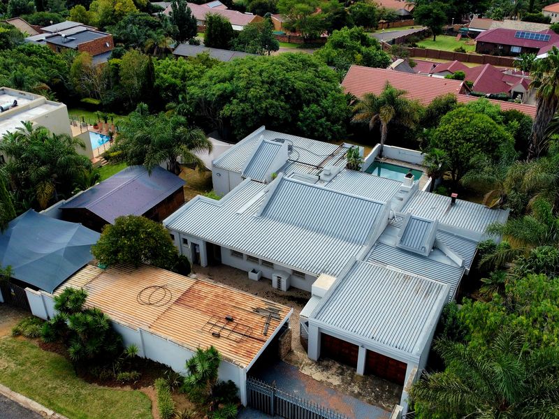 Aerial view of a residential property featuring a metal roof, swimming pool, and double garage within a landscaped suburban setting.
