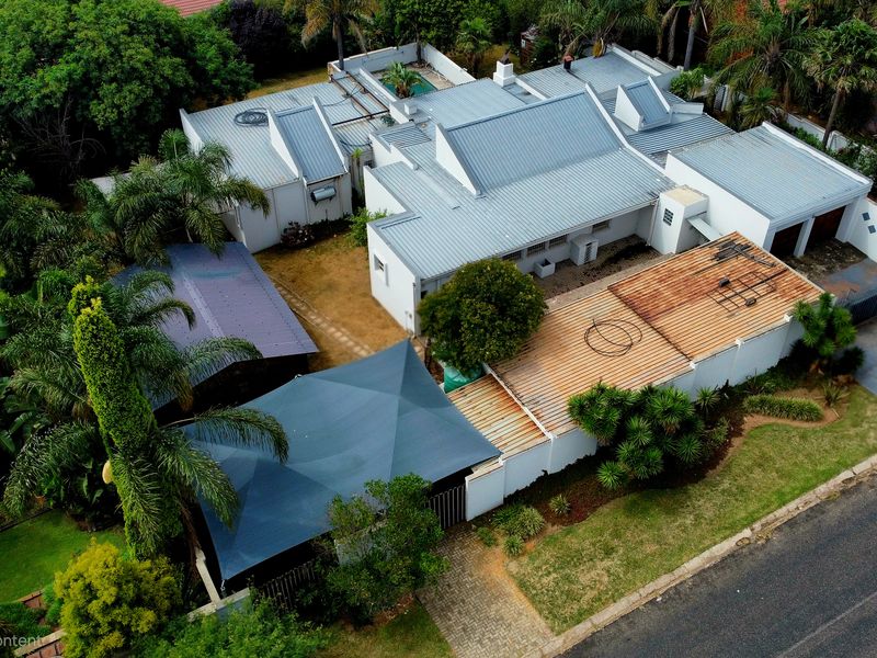 Aerial view of the property showcasing the roof structure, swimming pool, landscaped garden, and paved driveway area.