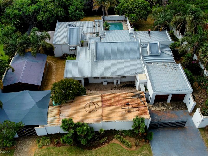 Aerial view of the property featuring a metal roof, swimming pool, double garage, and paved driveway set within a landscaped garden.
