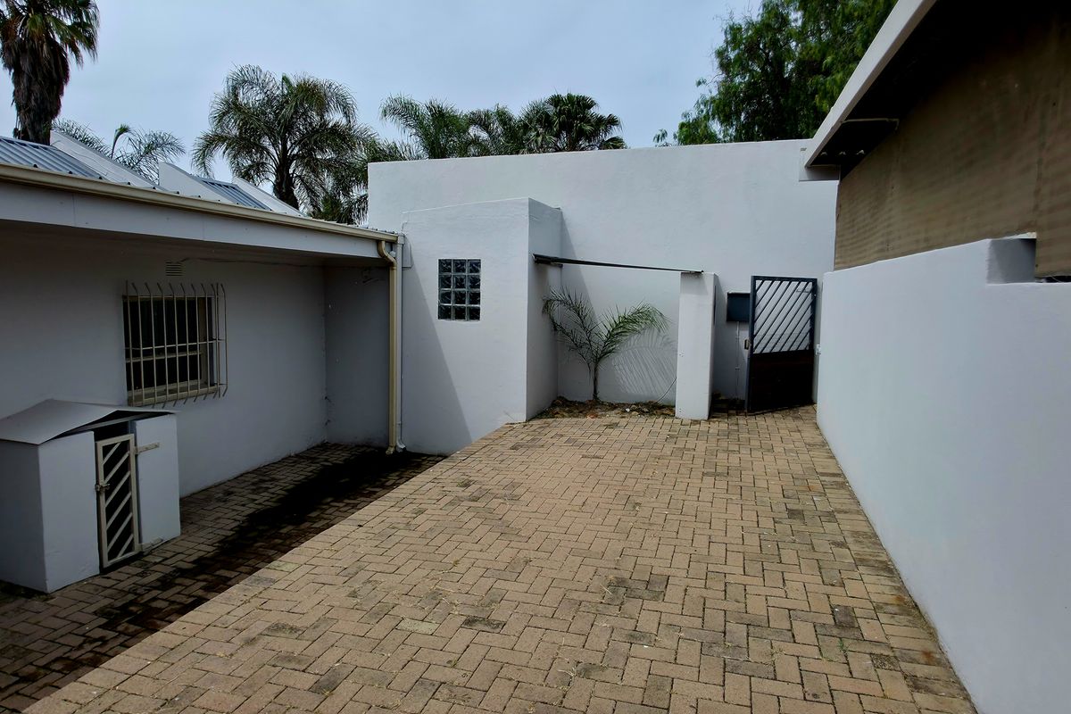 A paved rear courtyard area featuring security bars on windows, a glass block feature, and a metal access gate.