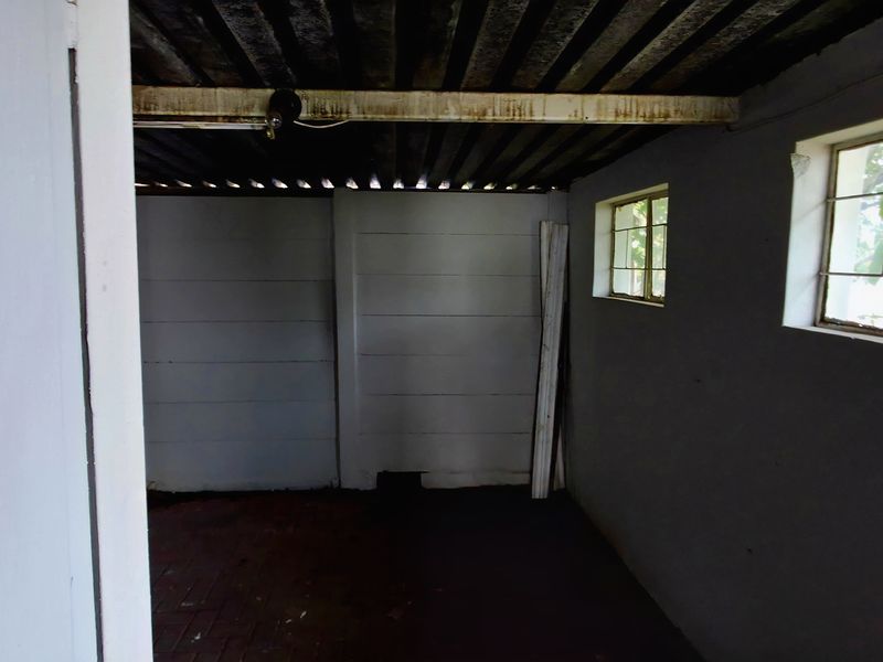 A basic, empty garage space featuring brick flooring, steel-framed windows, and an exposed corrugated metal ceiling, requiring maintenance and cosmetic updates.