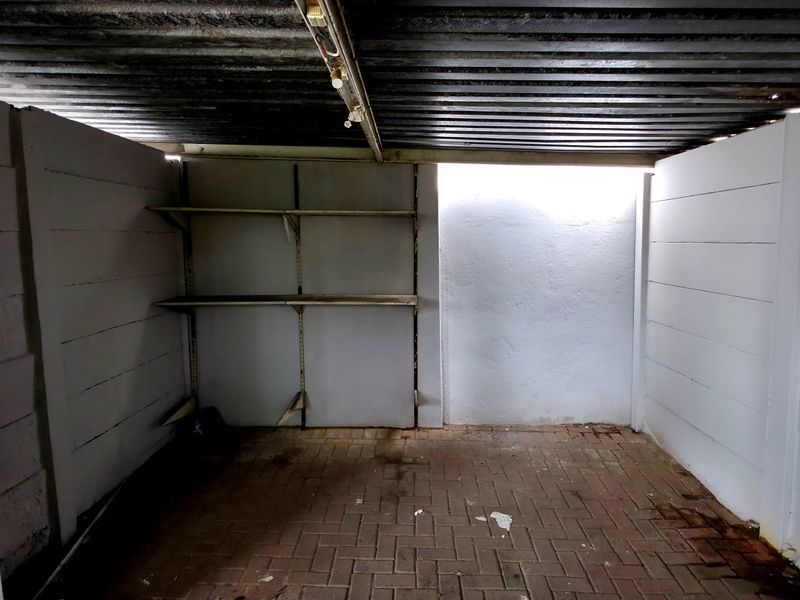 A basic, empty garage space featuring concrete block walls, a corrugated metal ceiling, and brick paved flooring with built-in storage shelving.