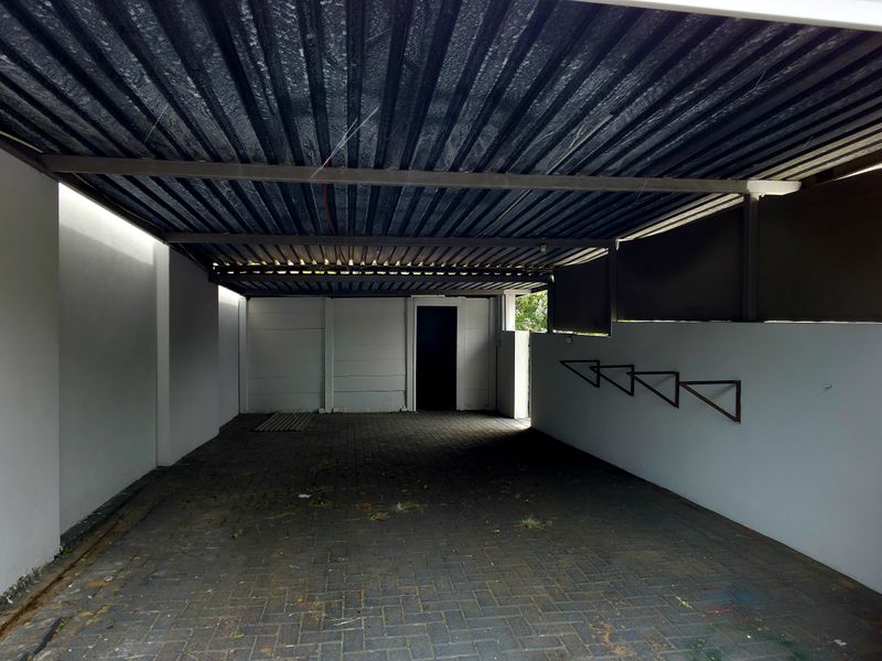 A covered outdoor parking area or garage featuring a corrugated metal roof, paved flooring, and stone-clad pillar detail.