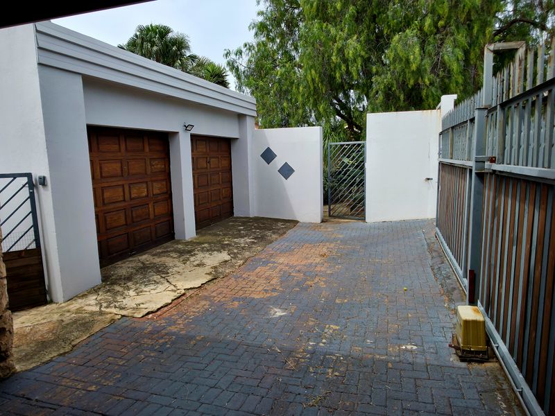 Front exterior view featuring a double garage, paved driveway, and secure perimeter fencing with gated access.