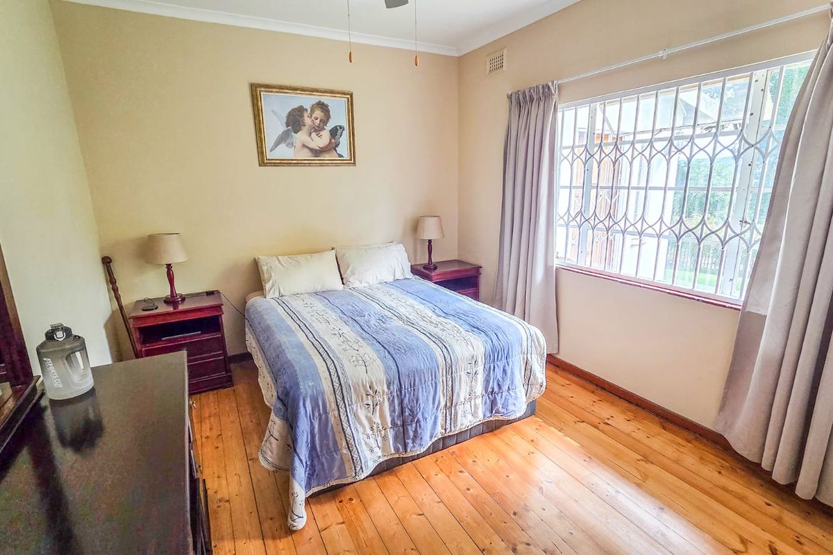 A bedroom featuring polished timber flooring, a large window with security bars, and neutral wall tones.