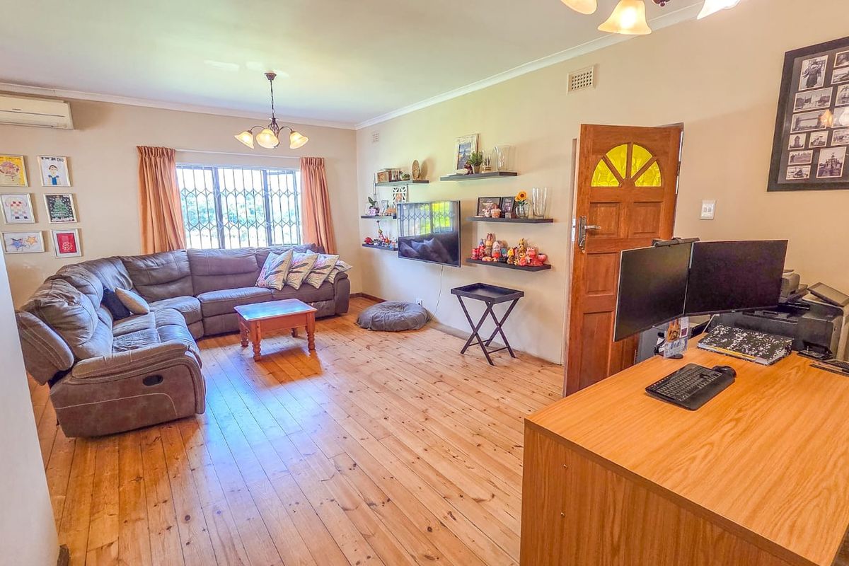 Spacious living area featuring polished timber flooring, a wall-mounted air conditioning unit, and a solid timber entrance door with decorative glass detailing.