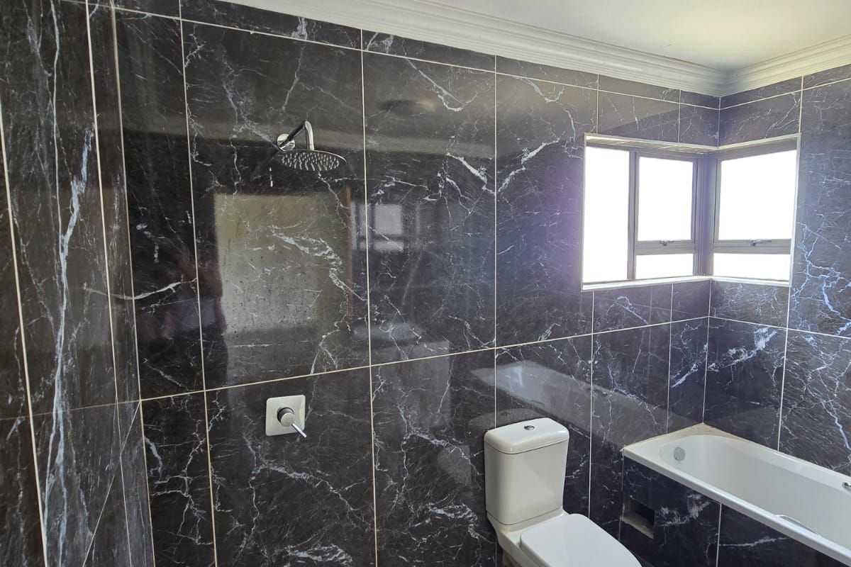 Modern bathroom featuring dark marble-effect wall and floor tiles, a built-in bathtub, a walk-in shower area, and a white ceramic toilet.