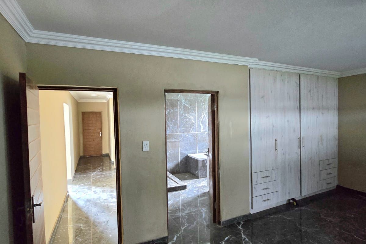 A bedroom featuring polished marble-look floor tiles, built-in wooden cupboards, and direct access to an en-suite bathroom and hallway.