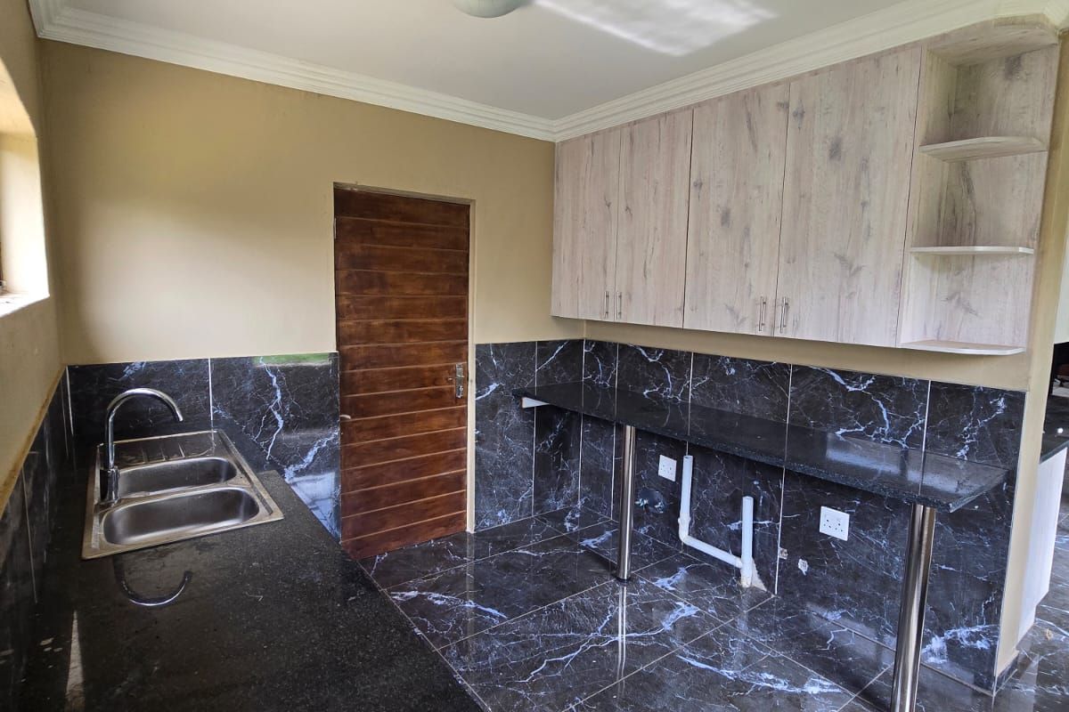 A modern kitchen featuring dark marble-effect tiled flooring and splashbacks, light wood-grain cabinetry, and a stainless steel double sink with granite countertops.