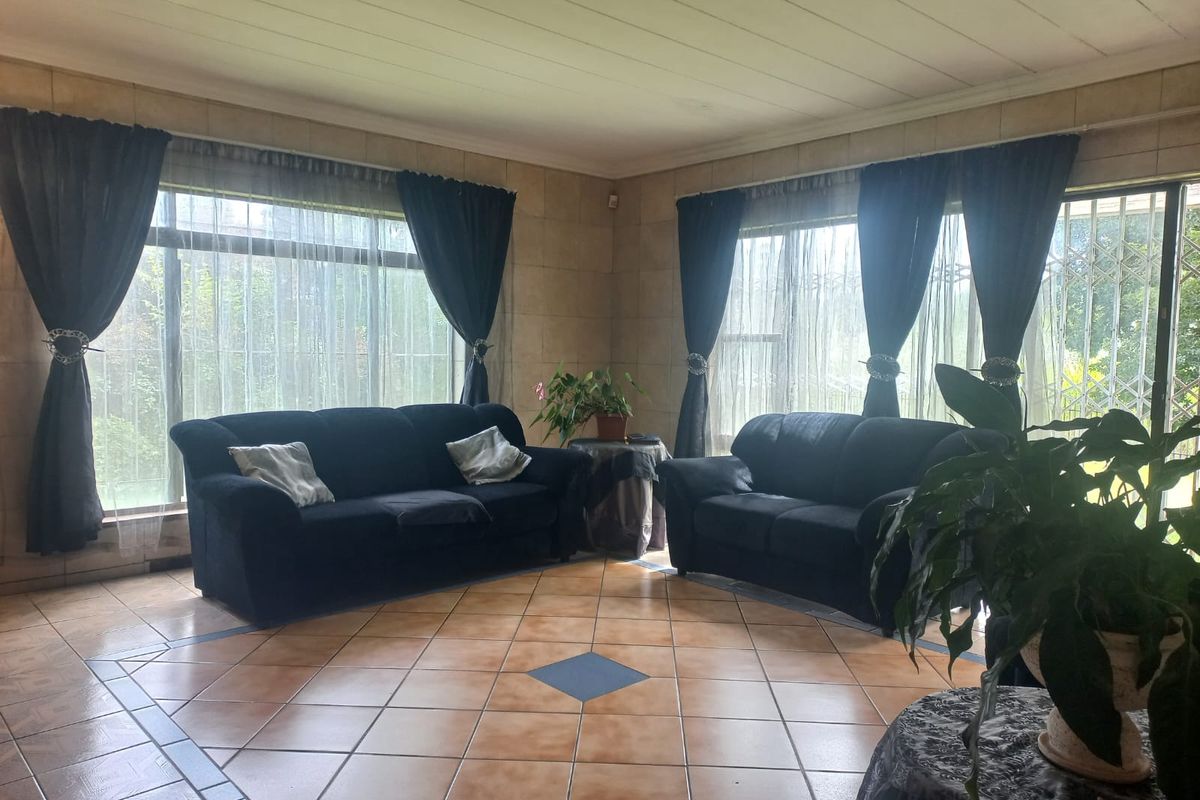 A spacious living room featuring large windows with security gates, tiled flooring, and neutral wall finishes, offering a bright and functional living space.