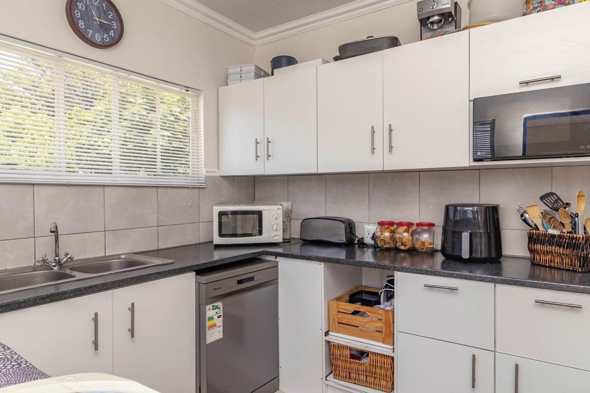 A functional kitchen featuring white cabinetry, dark laminate countertops, a double stainless steel sink, and tiled splashbacks with a window for natural light.