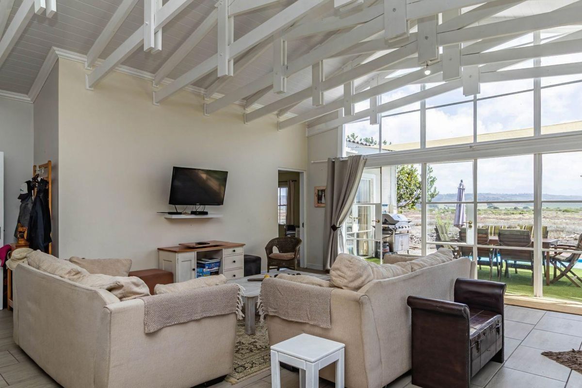 Spacious living room featuring high vaulted ceilings with exposed white beams, large floor-to-ceiling windows, and direct access to the outdoor patio area.