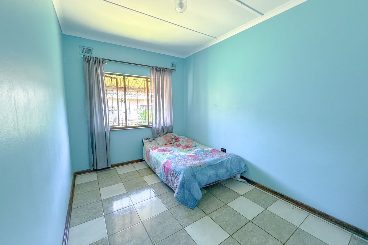 A simple bedroom featuring light blue walls, tiled flooring, and a window with security bars.