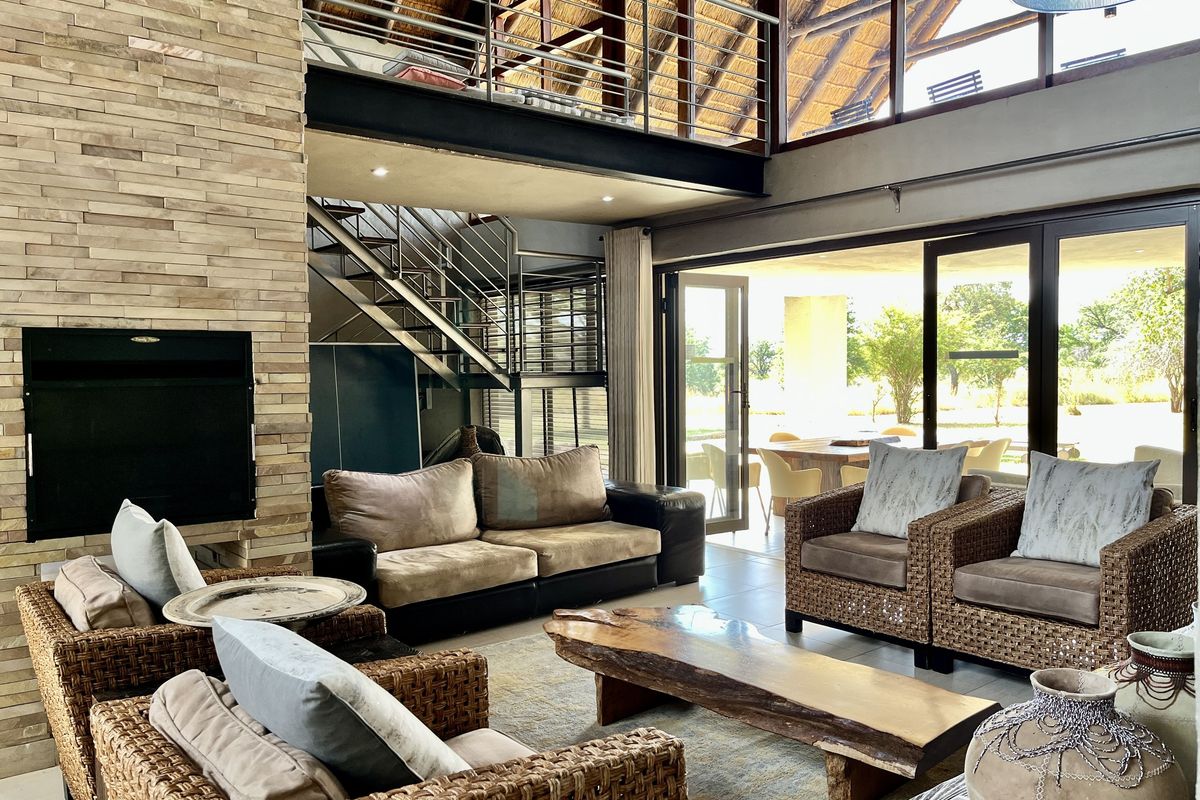 Spacious double-volume living area featuring a stone-clad fireplace, mezzanine level, and large glass sliding doors opening to an outdoor patio.