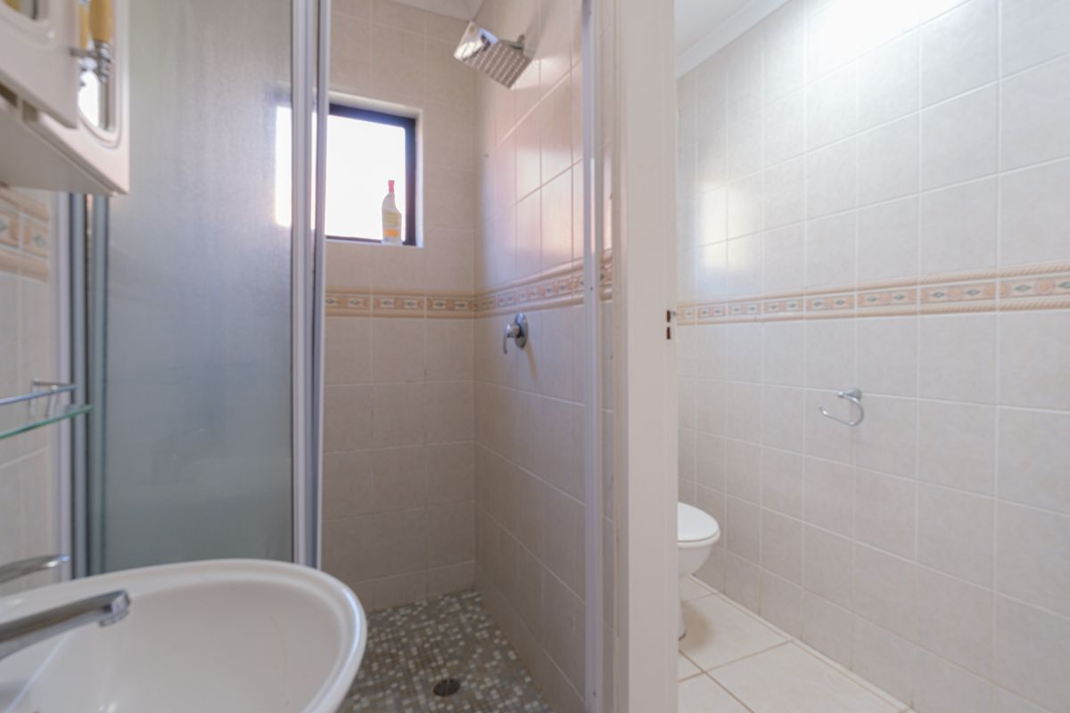 A functional bathroom featuring a tiled shower enclosure, pedestal basin, and a separate toilet area with neutral wall tiling.