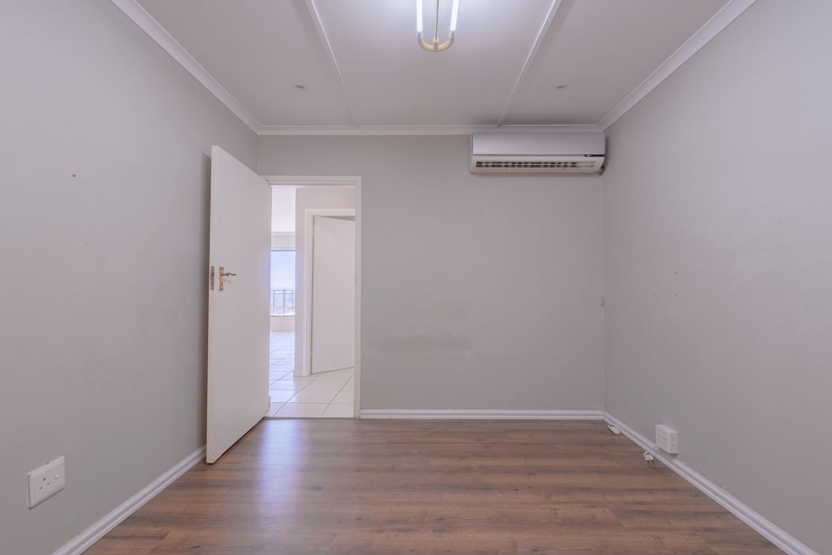 A neutral, empty bedroom featuring wood-look laminate flooring, a wall-mounted air conditioning unit, and access to an adjoining room.