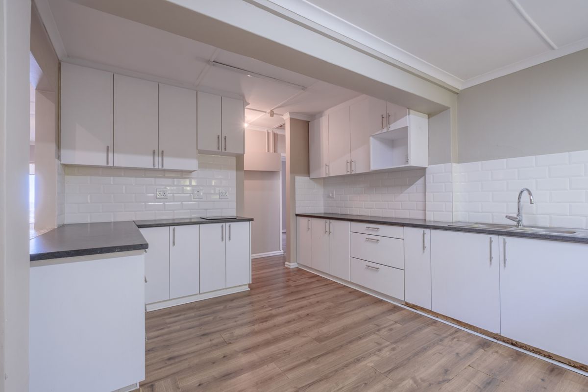 A clean, modern kitchen featuring white cabinetry, dark countertops, subway tile backsplash, and wood-look flooring.