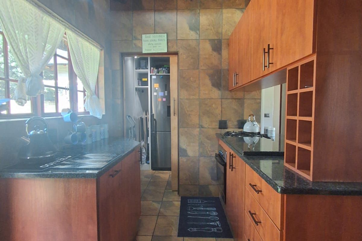 A galley-style kitchen featuring wooden cabinetry, granite countertops, and a distinctive thatched roof ceiling, with an adjacent scullery area.