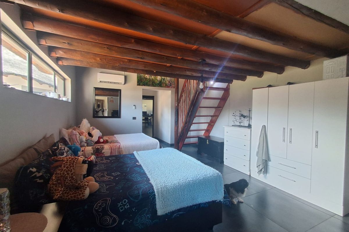 Spacious bedroom featuring exposed timber ceiling beams, tiled flooring, a split-system air conditioner, and a wooden staircase leading to an upper level.