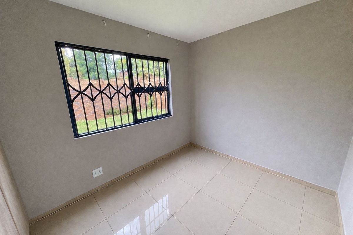 A clean, empty bedroom featuring neutral tiled flooring, smooth walls, and a window fitted with black security bars.