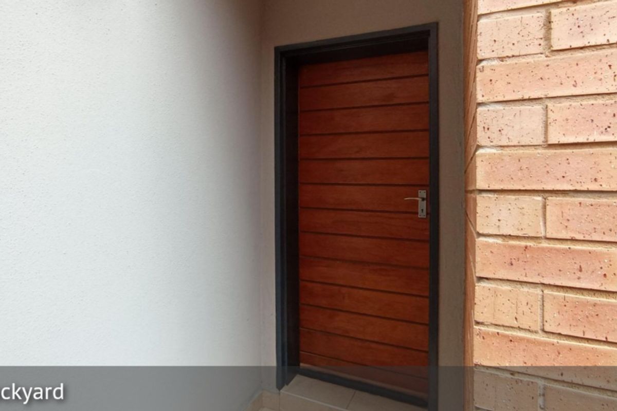 A view of a wooden exterior door leading into the property, set against a combination of plastered and face-brick wall finishes.