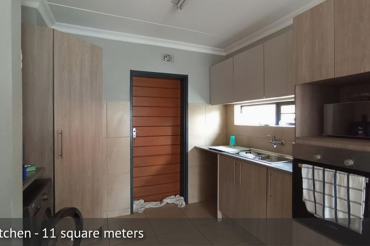 Functional kitchen featuring light wood-look cabinetry, built-in oven, stainless steel sink, and tiled splashbacks with direct access to an exterior door.