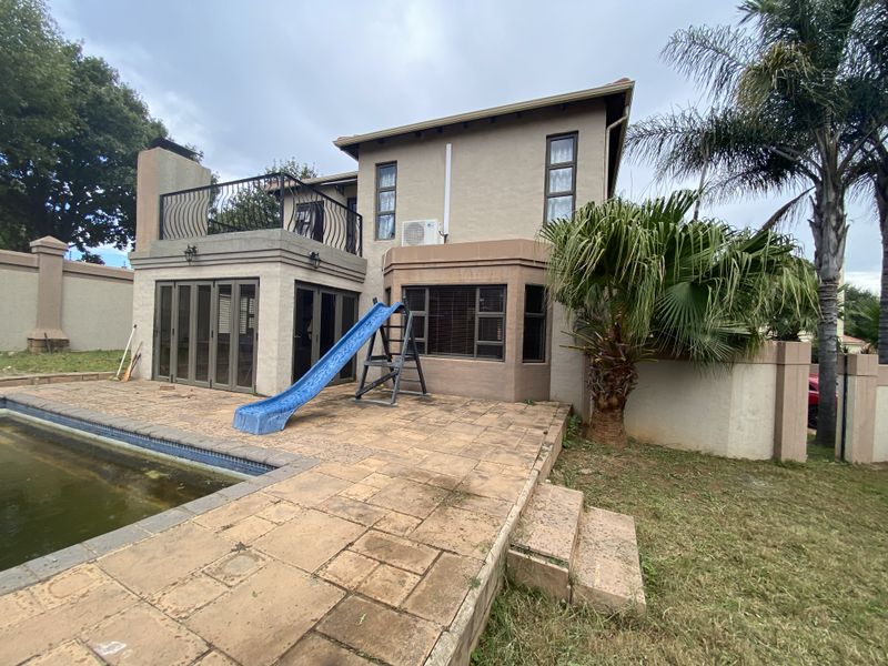 Rear view of the property featuring a swimming pool, paved patio area, and an upper-level balcony with wrought iron railings.